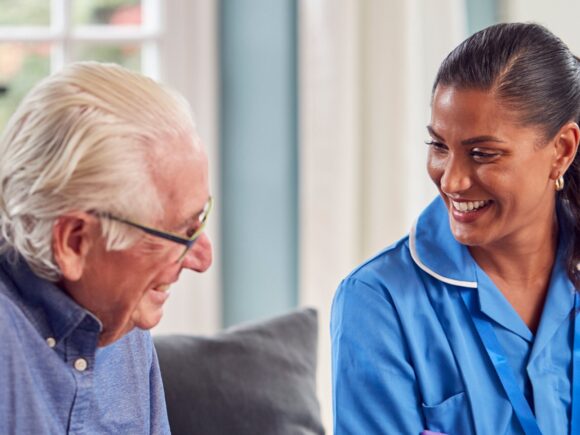 A nurse and her patient sit on a sofa and laugh together