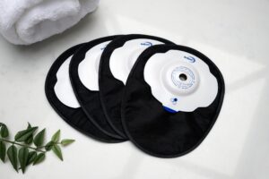 Four black closed Aura Plus Soft Convex stoma bags laid one on top of the other and fanned out on a white marble countertop.