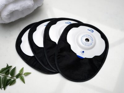 Four black closed Aura Plus Soft Convex stoma bags laid one on top of the other and fanned out on a white marble countertop.