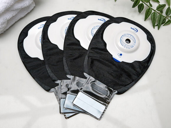 Four black Aura Plus Soft Convex drainable ileostomy bags stacked on top of each other and fanned out on a white marble countertop.
