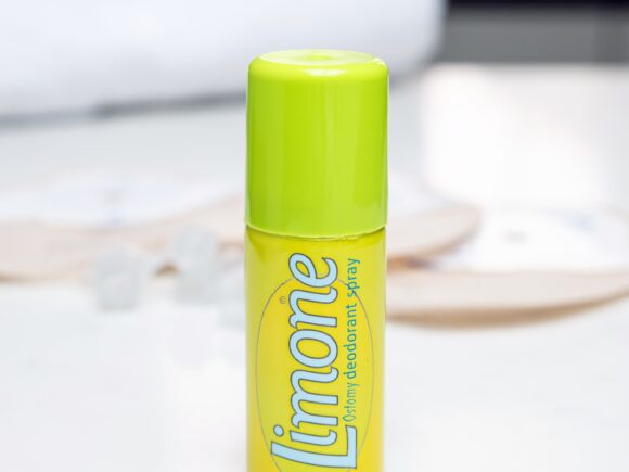 A bright yellow can of Limone ostomy deodorant spray on a white marble countertop, the objects in the background are blurred.