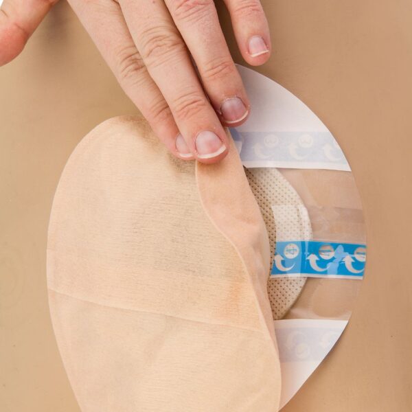 UltraFrame Flange Extenders on someone's skin and a hand pulling lifting the corner of the stoma pouch showing the flange extender