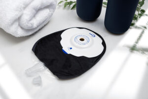 A black Aura Plus Soft Convex Urostomy bag with the valve open on a white marble worktop.