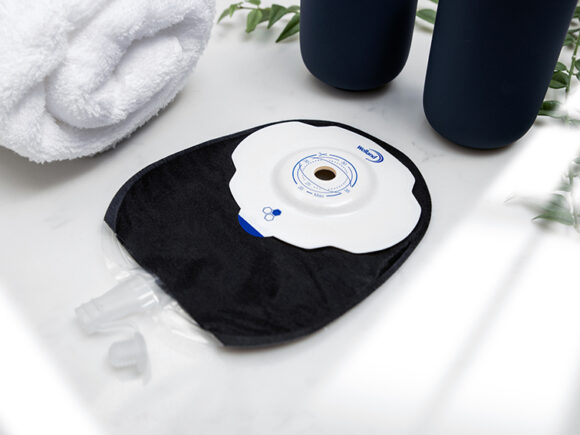 A black Aura Plus Soft Convex Urostomy bag with the valve open on a white marble worktop.