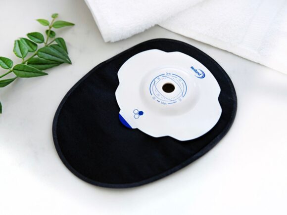 Photo of a black closed Aura Plus Soft Convex stoma bag with a white convex flange on a white marble countertop.