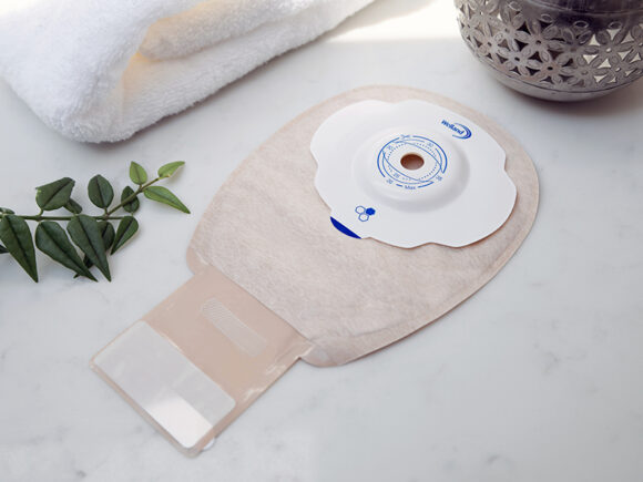 A sand coloured Aura Plus Soft Convex drainable ileostomy bag with the opening unfurled on a white marble worktop.