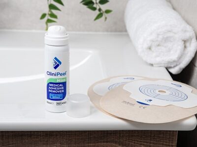 A can of CliniPeel with the lid off next to two sand Aura Plus stoma bags on the side of a sink