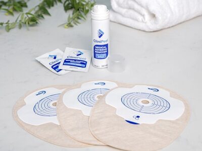 A can of CliniPeel with the lid off and two CliniPeel wipes in behind sand Aura Plus stoma bags
