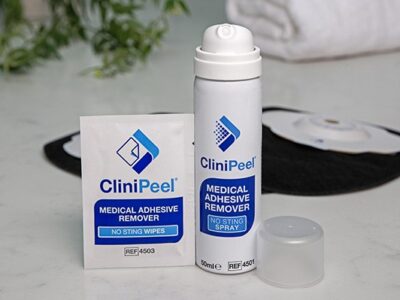 A can of CliniPeel with the lid off and a CliniPeel wipe in front of black Aura Plus Soft Convex stoma bags