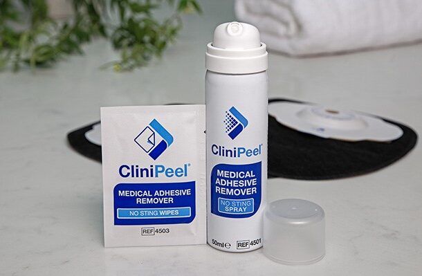 A can of CliniPeel with the lid off and a CliniPeel wipe in front of black Aura Plus Soft Convex stoma bags