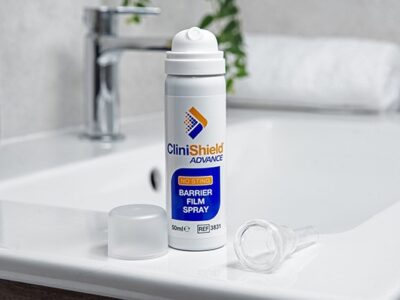 A can of CliniShield Advance spray with the lid off next to a CliniSure Urinary Sheath on the side of a sink