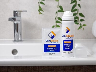 A can of CliniShield Advance spray with the lid off next to a a CliniShield Advance wipe on the side of a sink
