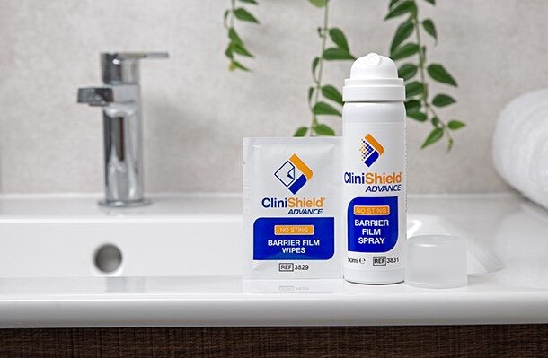 A can of CliniShield Advance spray with the lid off next to a a CliniShield Advance wipe on the side of a sink