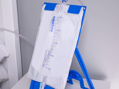 A CliniSure sterile night drainage bag on a blue plastic stand on a bedside table.