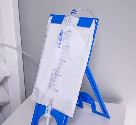 A CliniSure night drainage catheter bag setup on a night stand