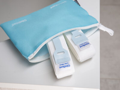 Two CliniSure retaining straps sticking out of a zip-up wash bag sat on the corner of a bath.