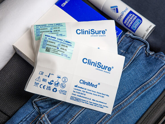 A packaged CliniSure sheath on top of its box next to a can of CliniPeel on top of folded clothes in a suitcase.