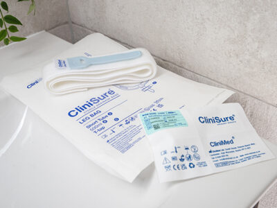 A CliniSure sheath package, a CliniSure retaining strap and a CliniSure leg bag in its packaging on the side of a sink.