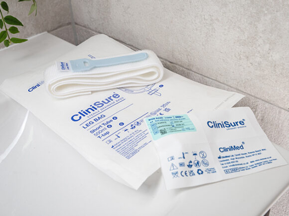 A CliniSure sheath package, a CliniSure retaining strap and a CliniSure leg bag in its packaging on the side of a sink.