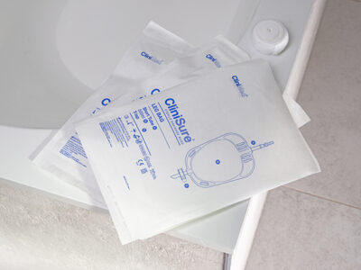 Three CliniSure leg bags in their packaging stacked on the corner of a bath.