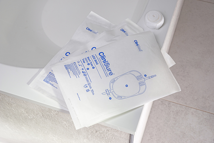Three CliniSure leg bags in their packaging stacked on the corner of a bath.