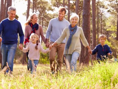 A family walk through woodland, the grandparents lead the way holding the children's hands while the parents walk behind.