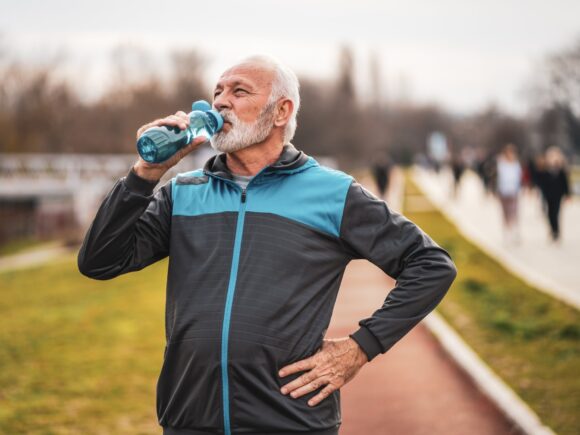 An older man drinks from a water bottle, he appears to have just finished running in the park.