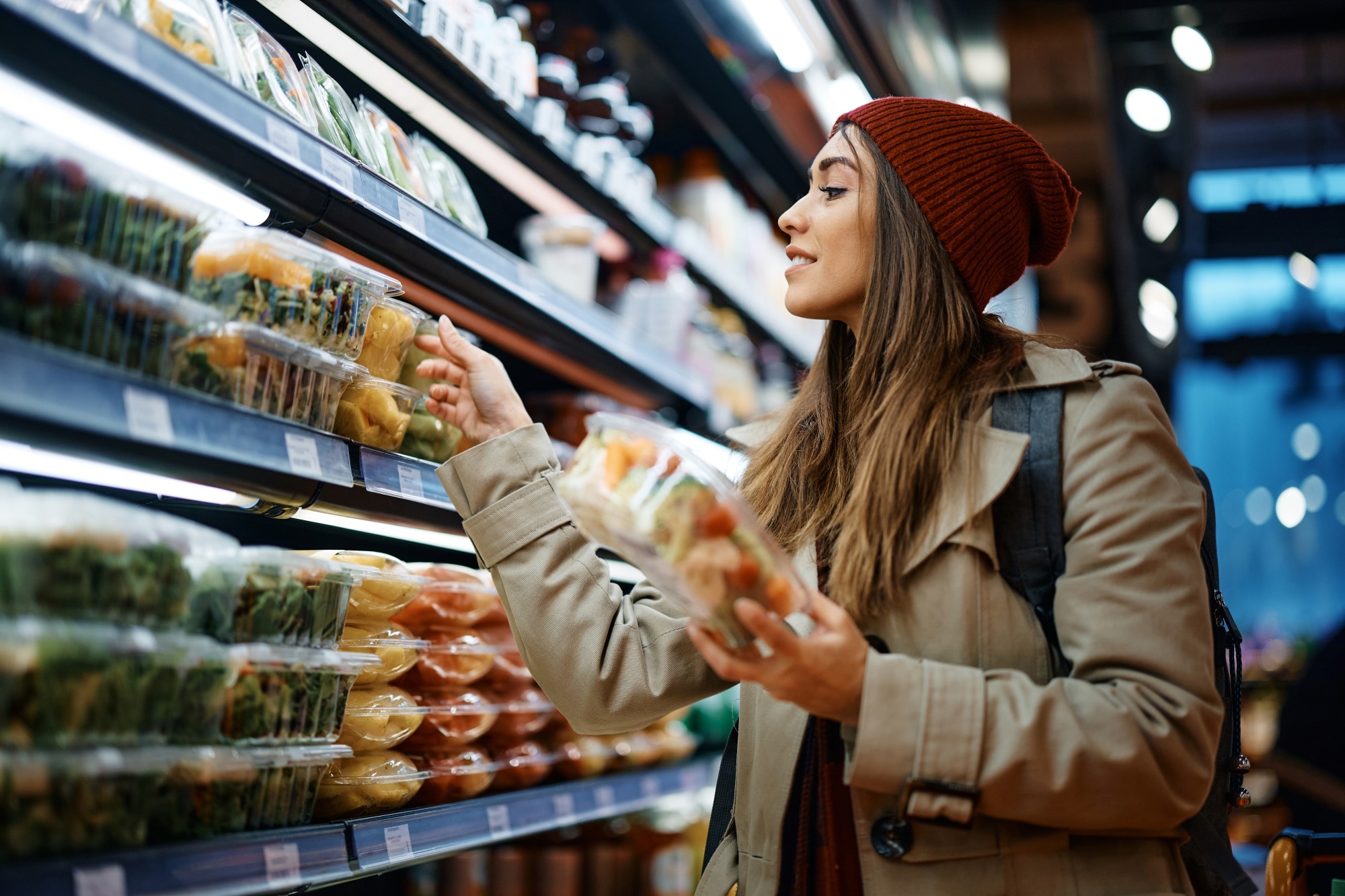A woman looks at boxes of prepared salad and fruits on the shelves of a supermarket.
