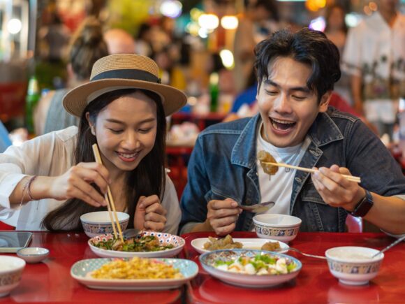 A young Asian couple enjoy a selection of Chinese dishes with chopsticks.