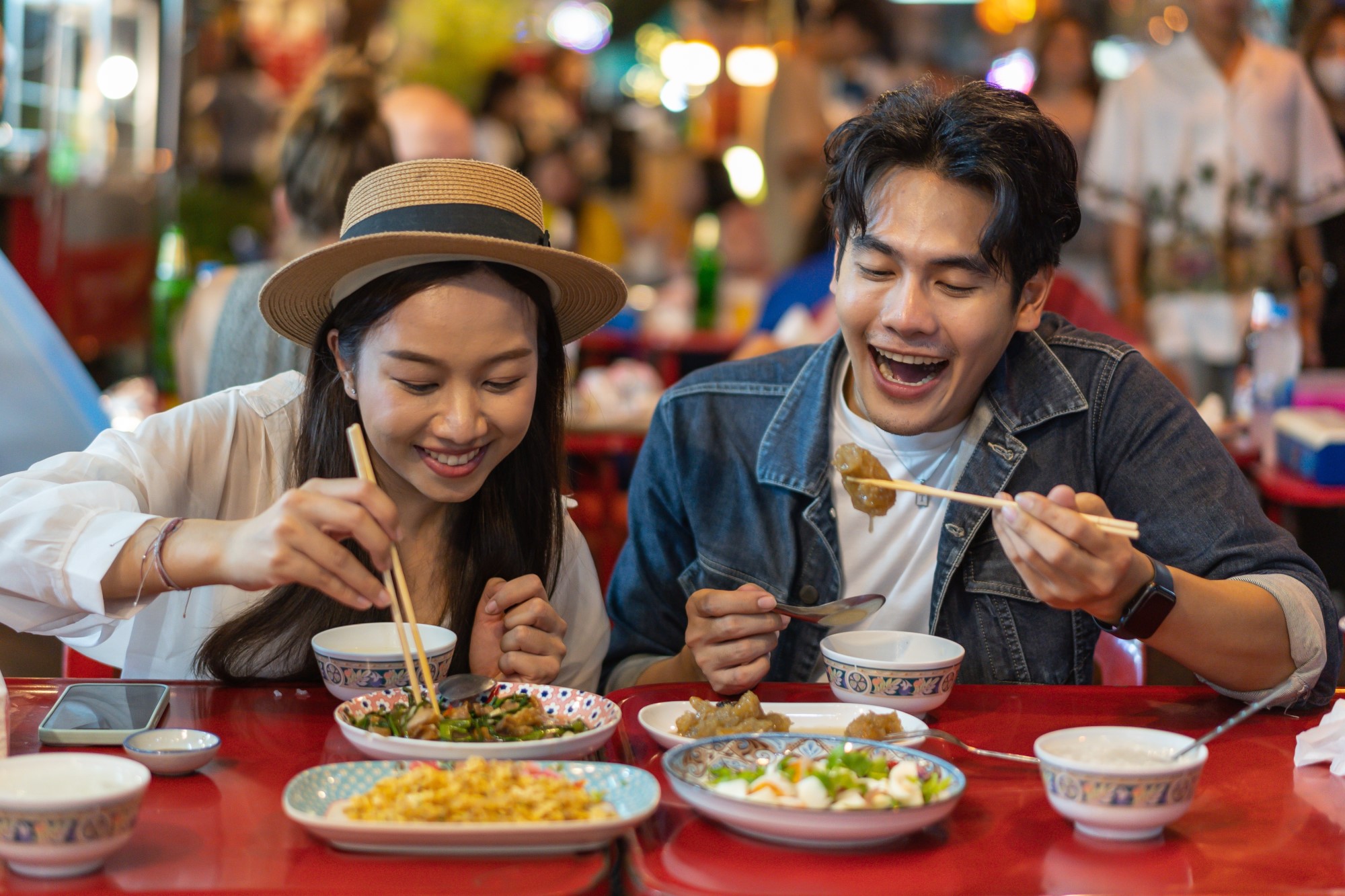 A young Asian couple enjoy a selection of Chinese dishes with chopsticks.