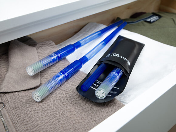 Three Curan man catheters with one in Curan wallet laying on some shirts in a drawer.