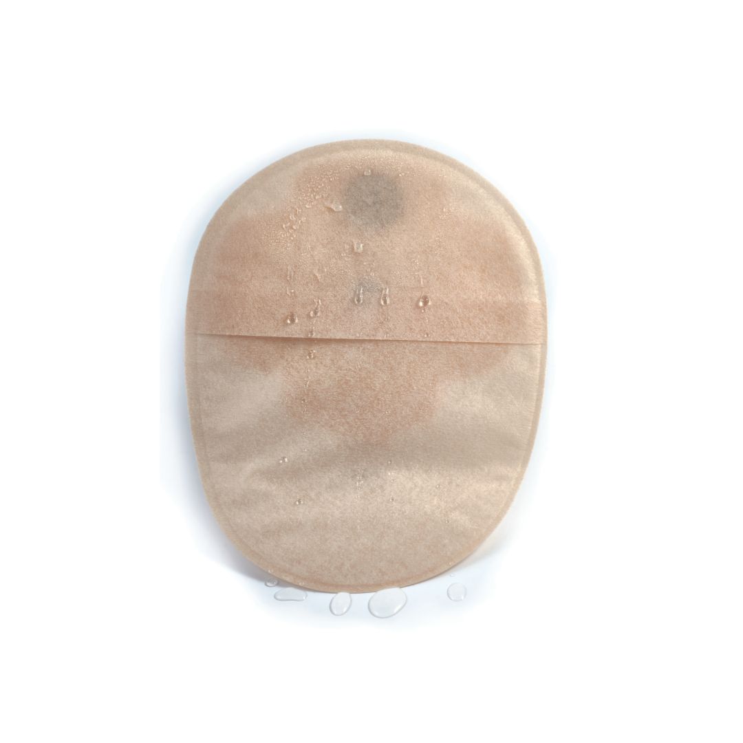 The back of a sand Aura Plus closed stoma bag with water droplets running down it's waterproof surface.