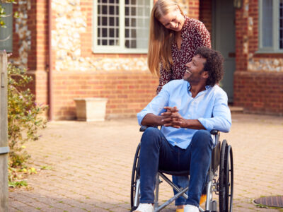 A man in a wheelchair smiles at a woman who is standing behind him.
