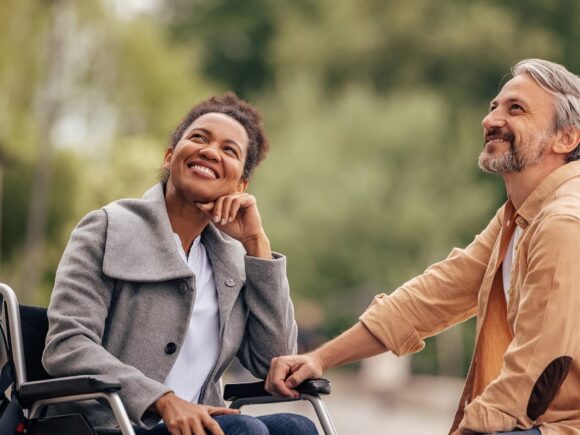 A woman in a wheelchair and a man sat in front of her look upwards smiling.