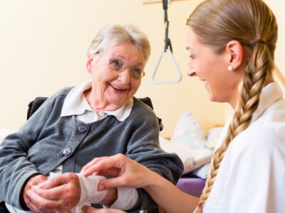 A nurse tends to a dressing on an older woman's wrist, they smile at each other and laugh.