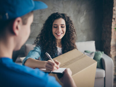 A woman signing for a package from a delivery man dressed in blue.