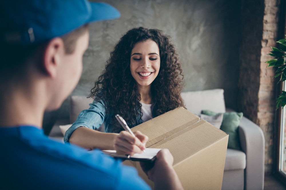 A woman signing for a package from a delivery man dressed in blue.