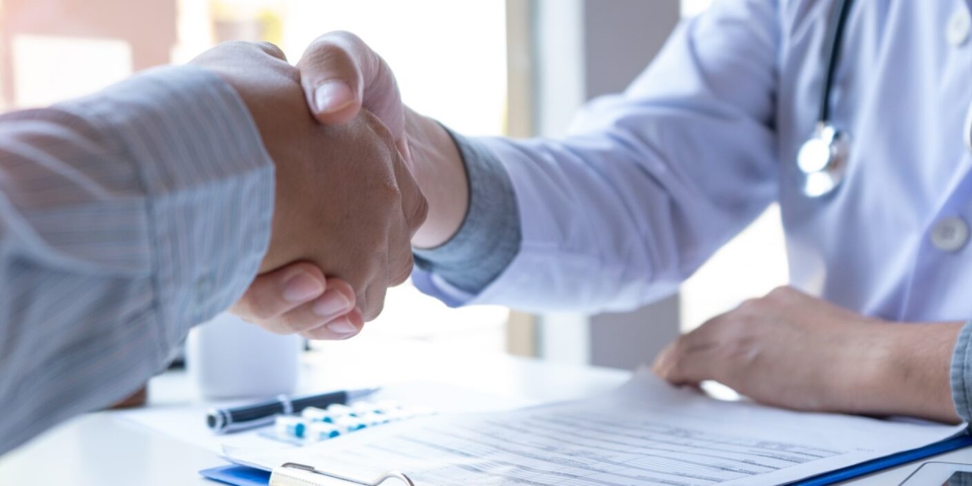 Close up of two people shaking hands, one of them is a doctor.