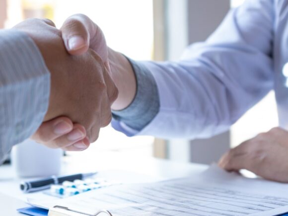 Close up of two people shaking hands, one of them is a doctor.