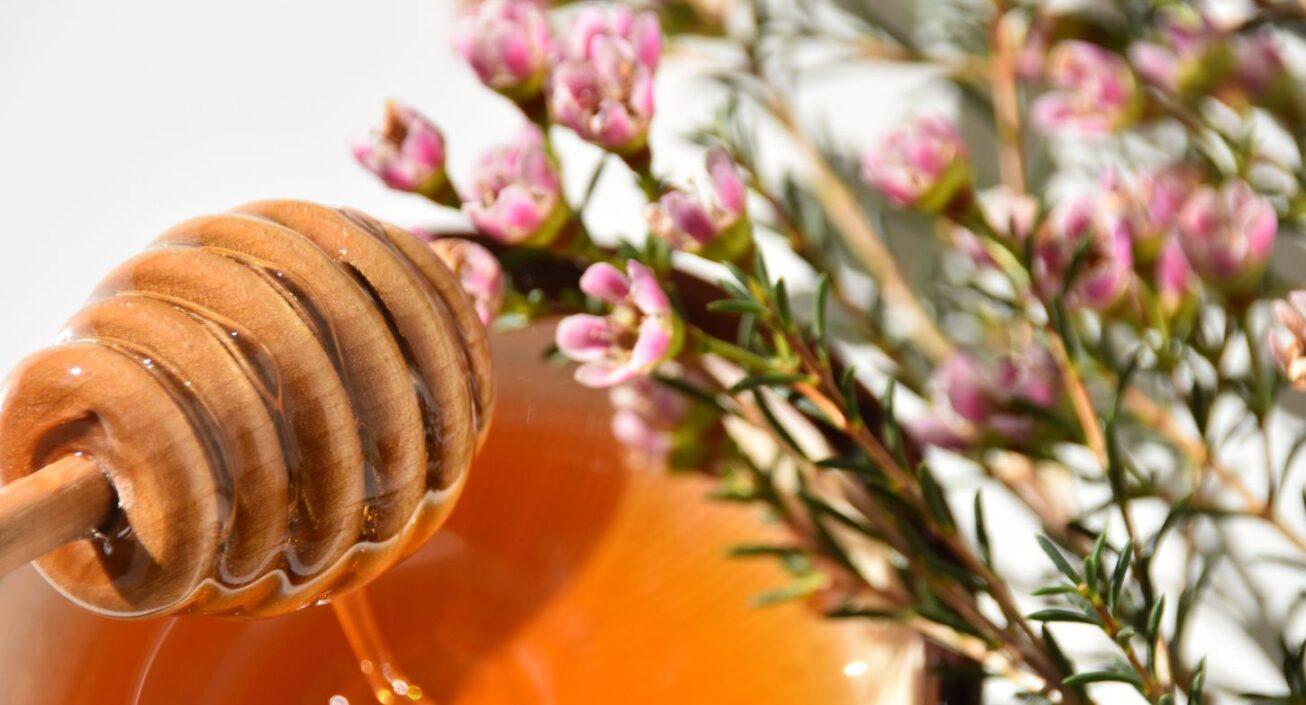 A bunch of Manuka flowers next to a bowl with honey dripping into it from a wooden dipper.