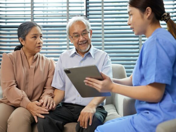 A nurse sits with an older couple and shows them something on a tablet.