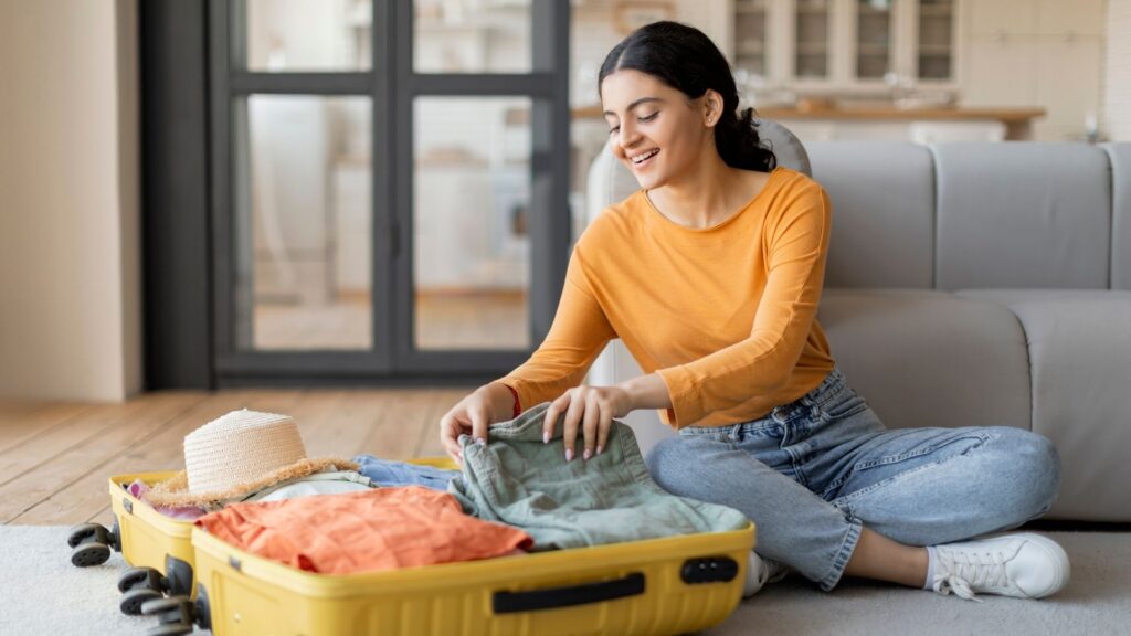 Photo of a lady sat on her floor packing her suitcase.