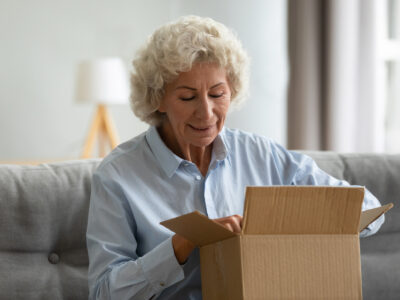 Mature lady smiling whilst opening a parcel at home on her sofa