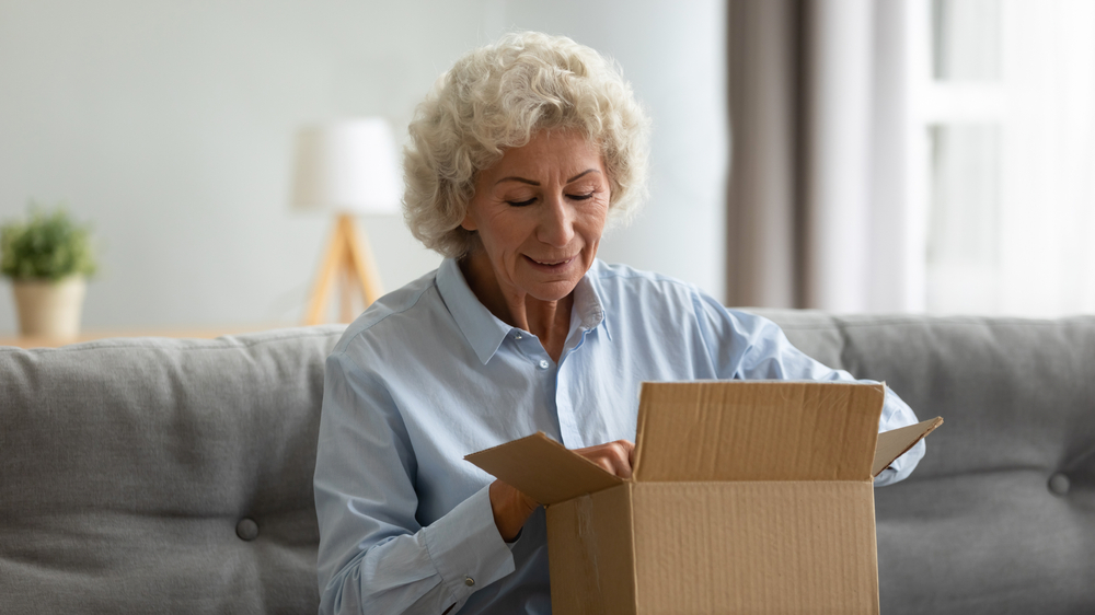 Mature lady smiling whilst opening a parcel at home on her sofa