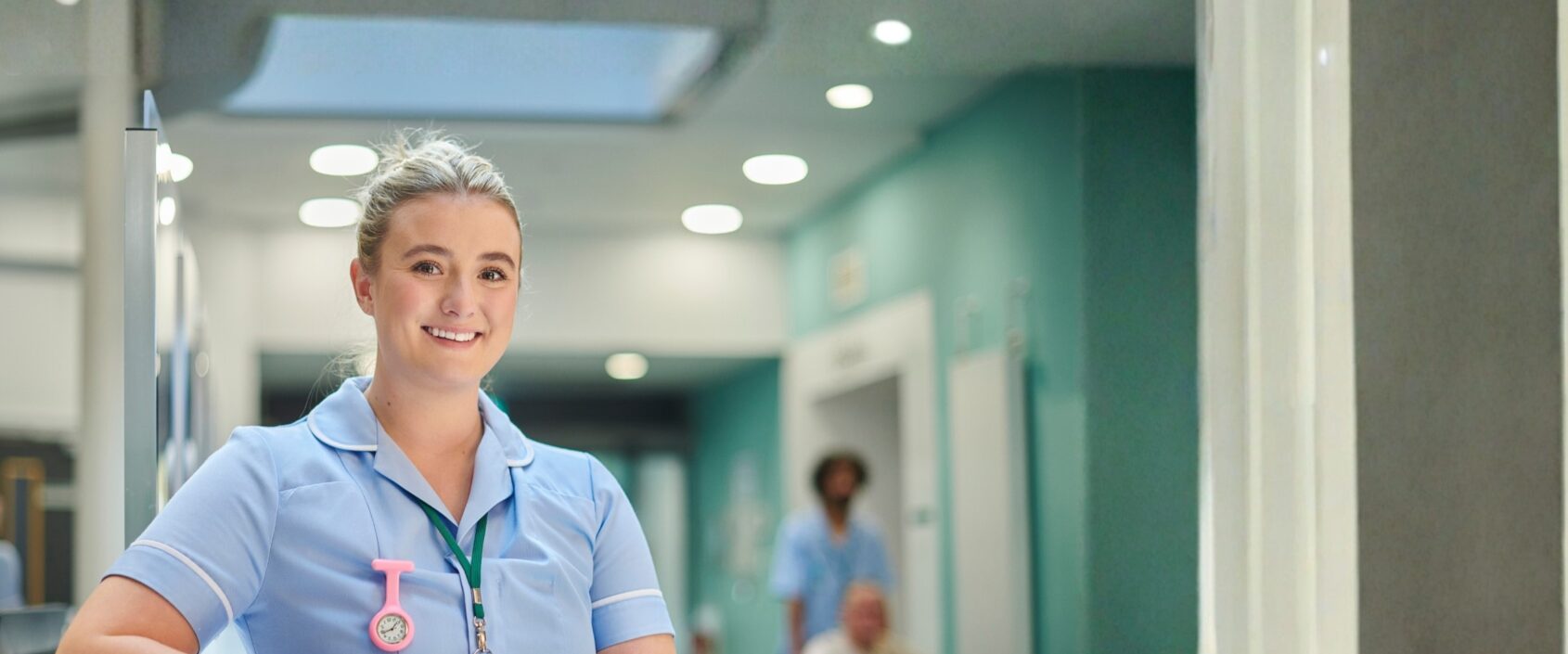 Photo of a nurse standing smiling in a hospital setting.