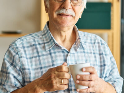 Photo of a elderly man looking towards the camera holding a mug.