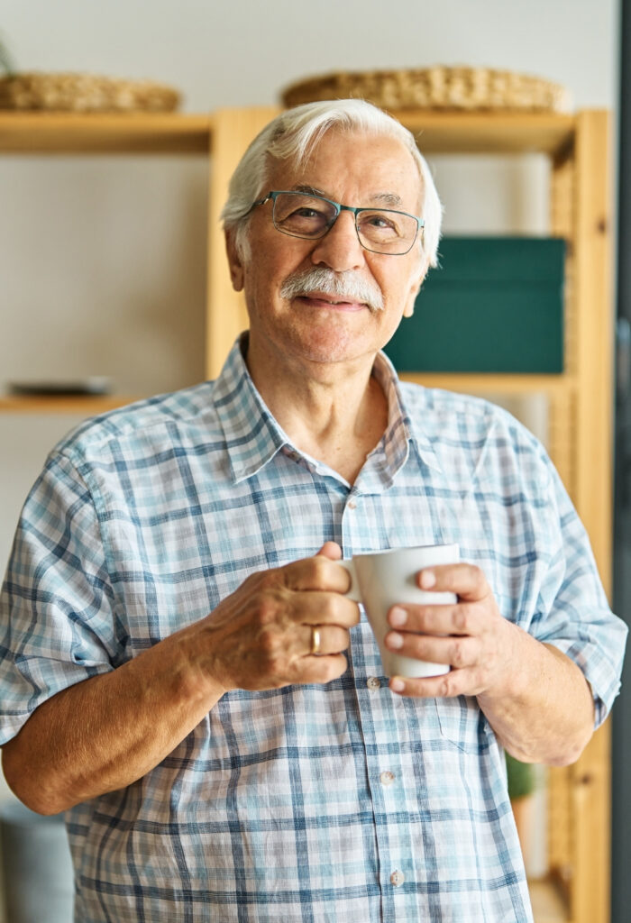 Photo of a elderly man looking towards the camera holding a mug.