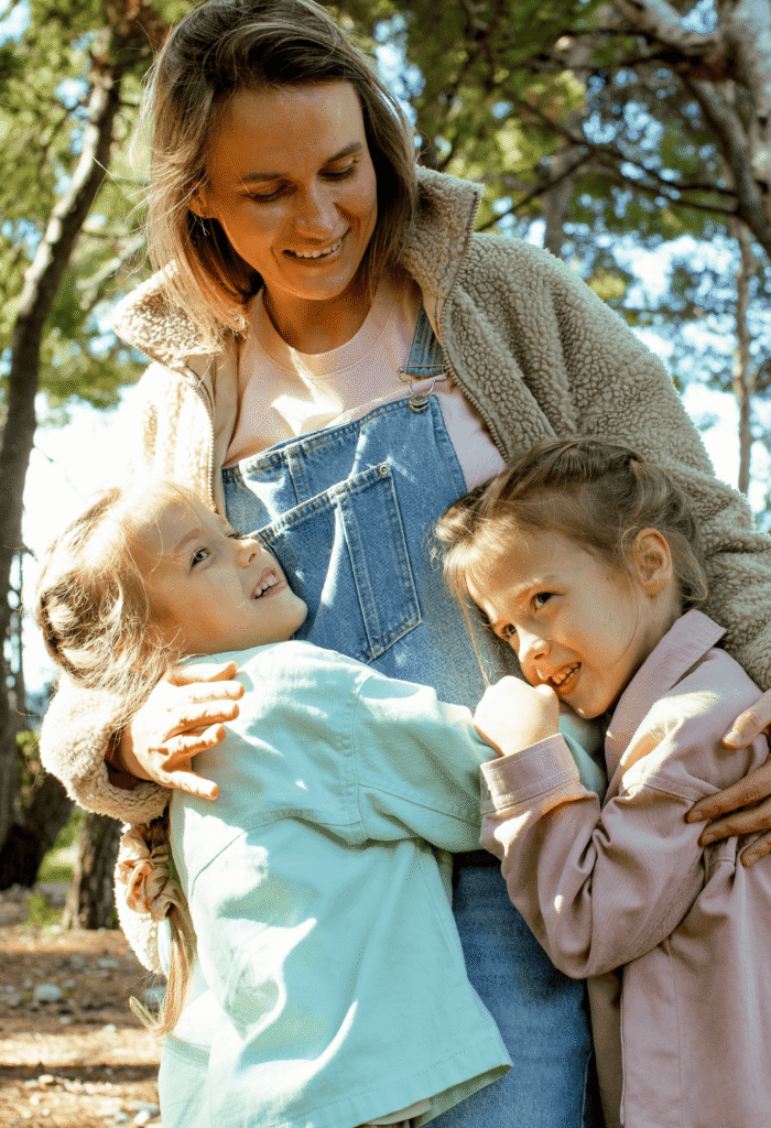 Photo of a mum standing outside hugging her two young daughters.