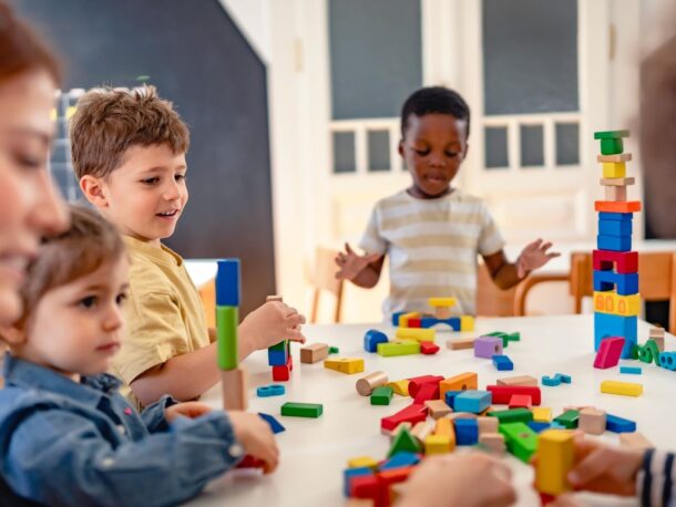 Photo of children sitting around a table playing with building blocks.