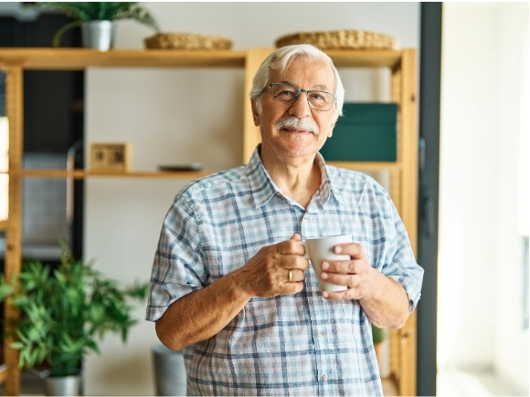 Photo of a elderly man looking towards the camera holding a mug.